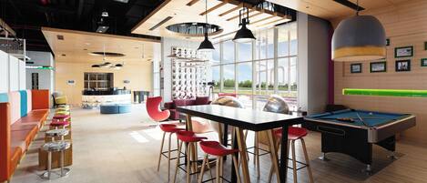 Un espace intérieur moderne doté d’une table de billard, de chaises rouges et d’un coin bar.