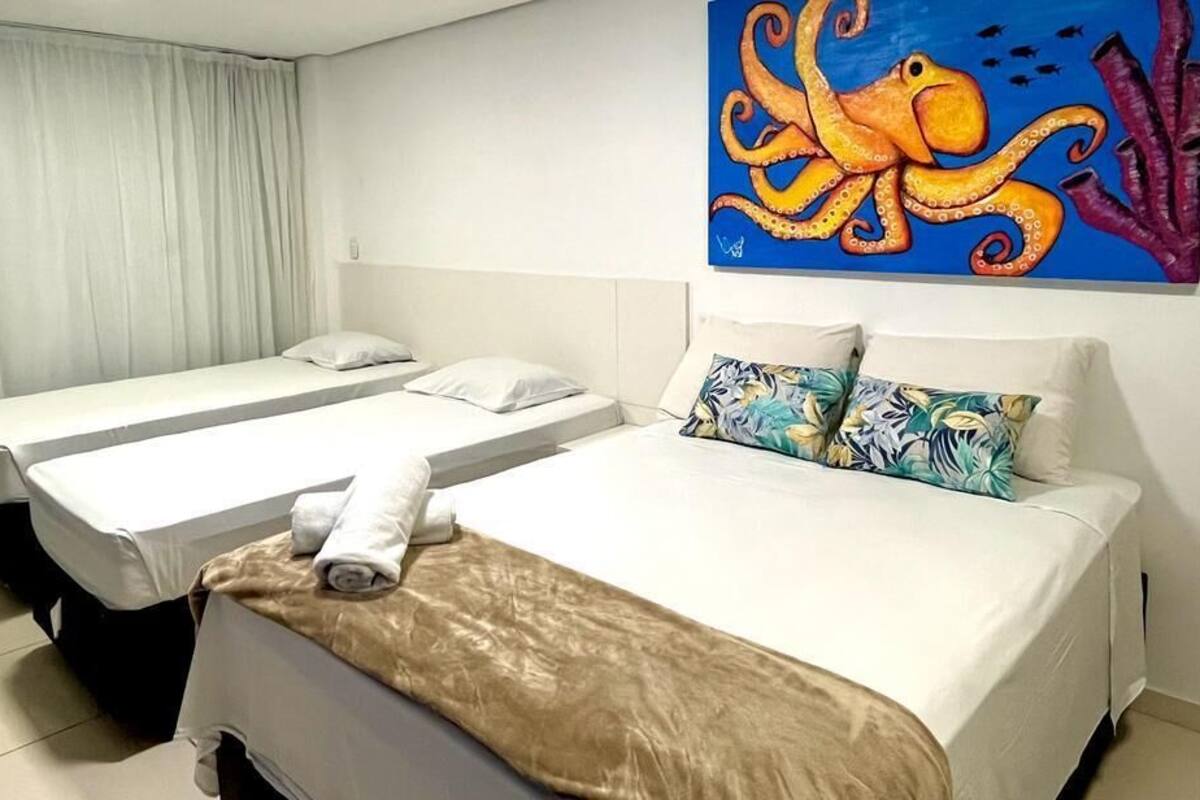 A hotel room with two single beds, a large painting of an octopus, and a view of the sea through the window.