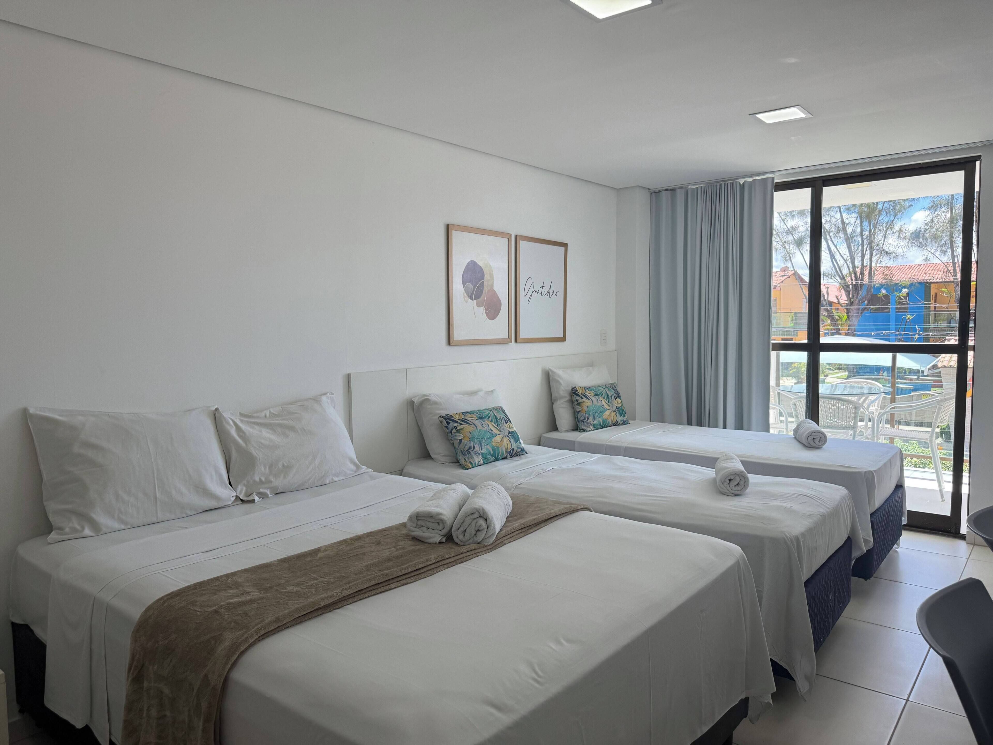 A hotel room with two beds, a large window with a view, and a ceiling light.