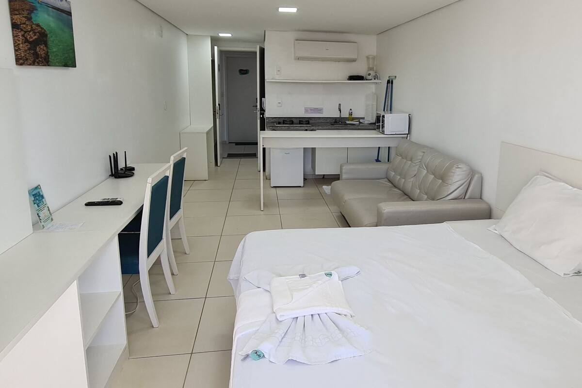 A hotel room with a bed, a desk, a chair, a sofa, and a kitchenette.