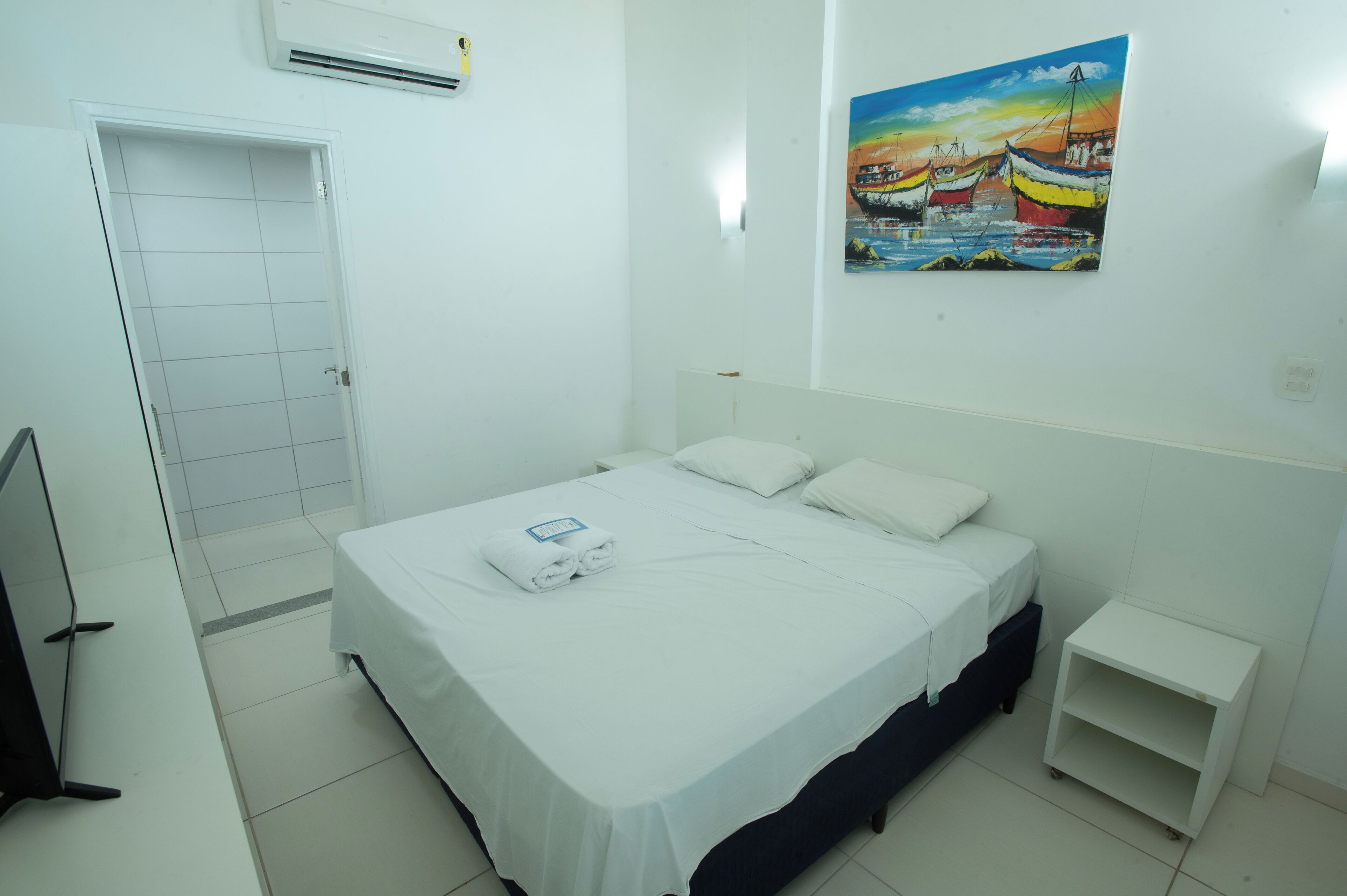 A hotel room with a bed, a small bedside table, a door, and a painting on the wall.