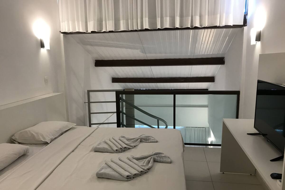 A modern hotel room with a bed, a TV, and a view of a balcony.