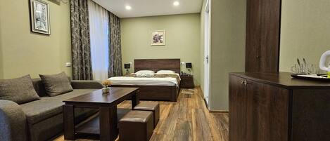 A hotel room with a bed, a sofa, a small table, a cabinet, and a painting on the wall.