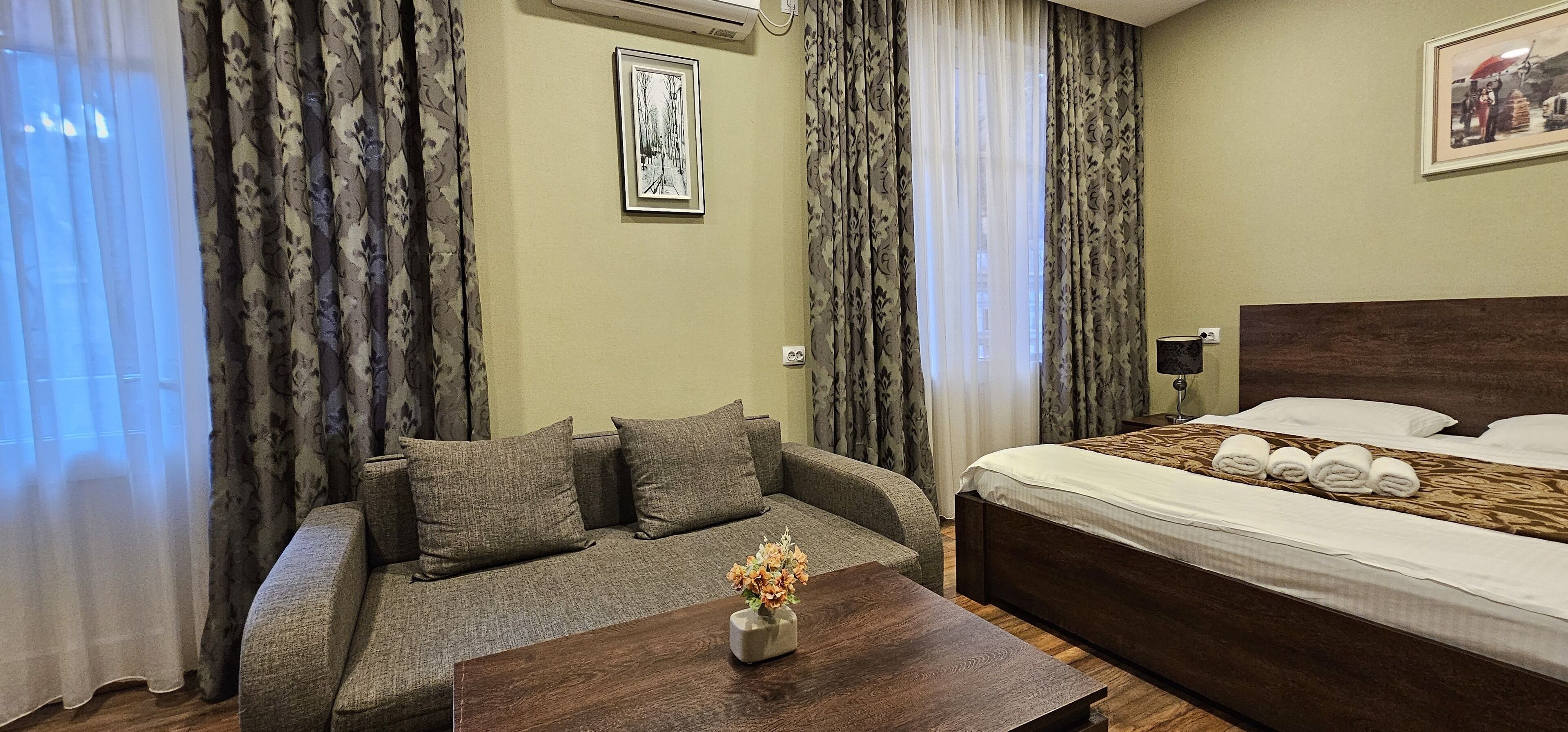 Une chambre d’hôtel avec un canapé, un lit, une table basse en bois et un tableau encadré au mur.