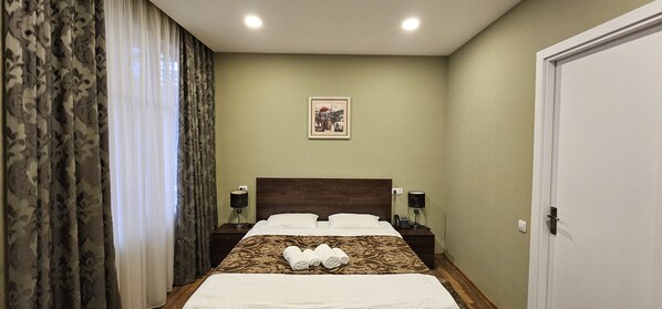 Une chambre d’hôtel avec un lit, deux tables de chevet avec des lampes, un tableau encadré au mur et une porte.