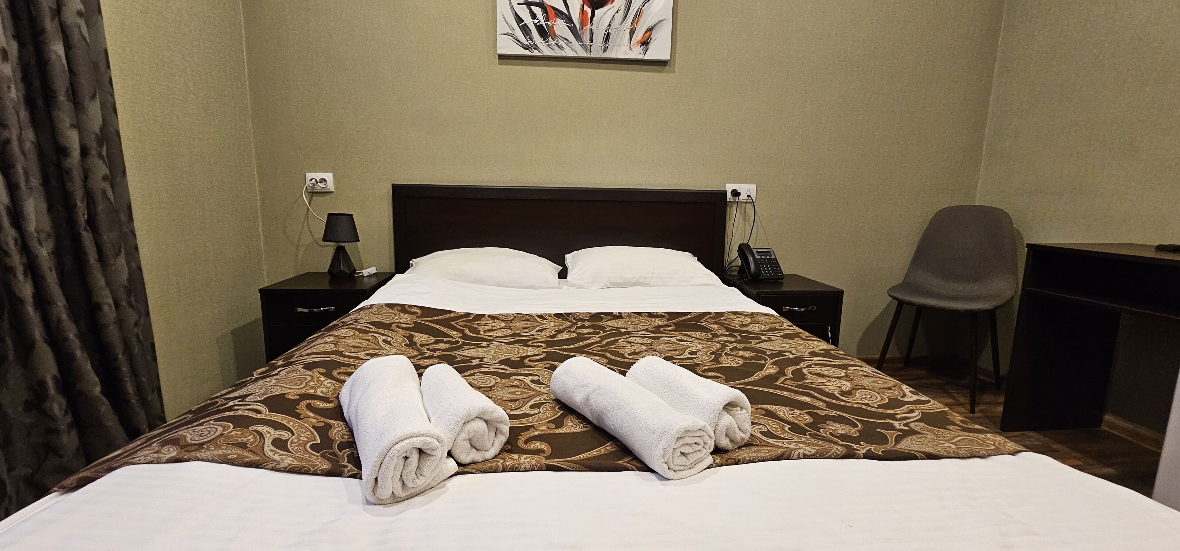 Une chambre d’hôtel avec un grand lit, deux tables de chevet avec des lampes, un bureau avec une chaise et un tableau au mur.