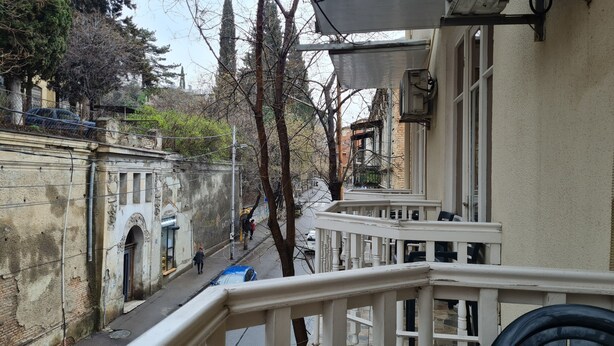 Une rue étroite, bordée de bâtiments des deux côtés, avec un piéton et une voiture bleue.