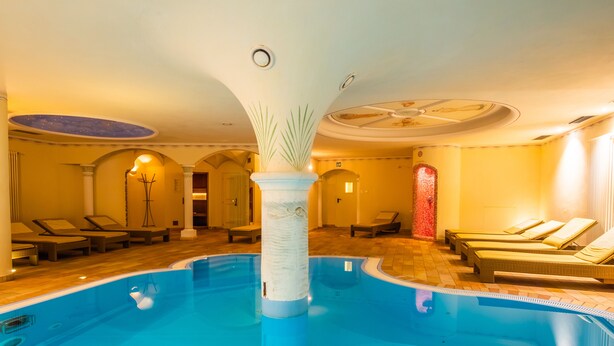 An indoor swimming pool with lounge chairs and a decorative pillar. - Hotel & Restaurant Feldrand (Sarentino)