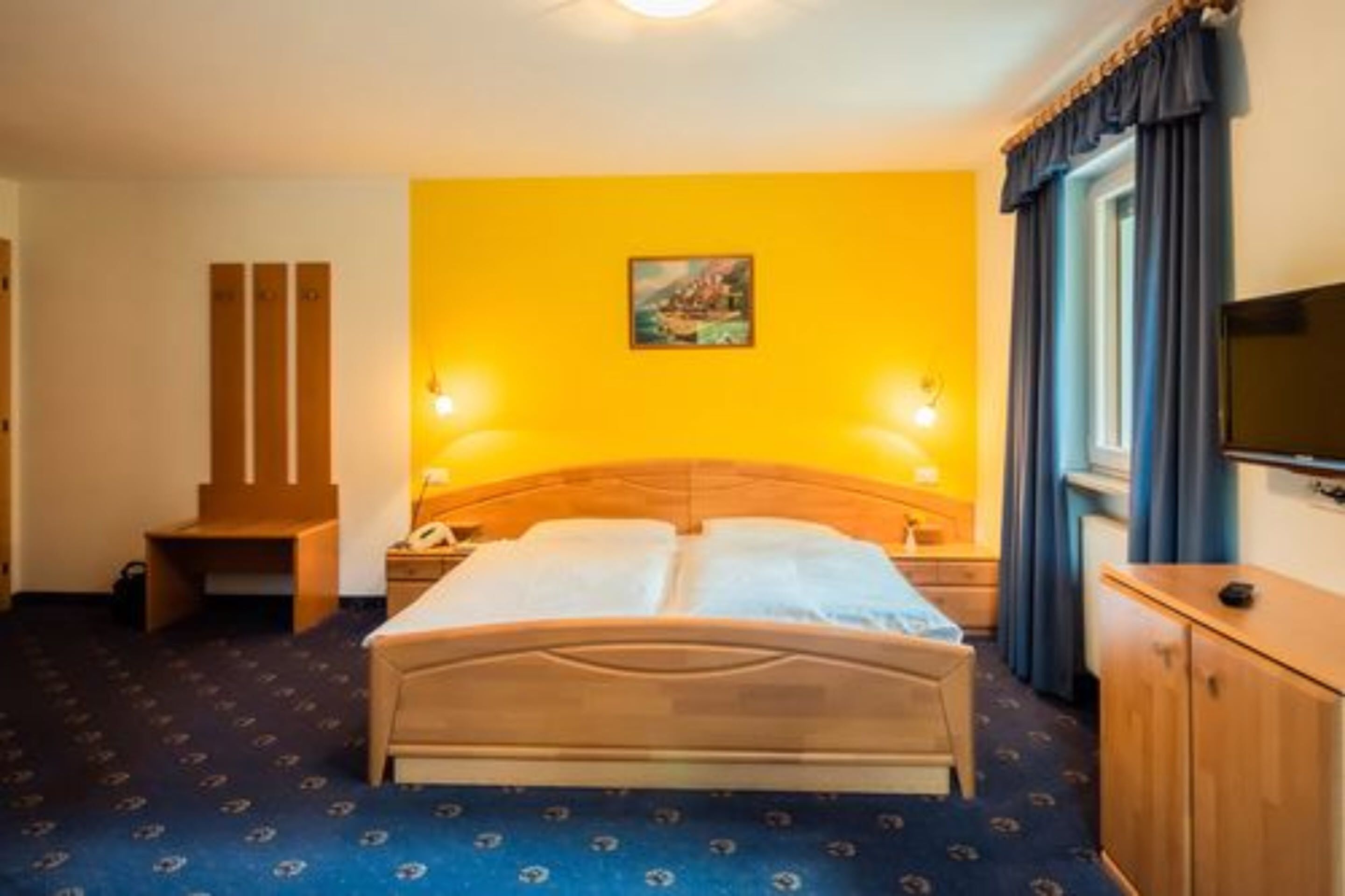 Habitación de hotel con cama, lámparas de noche, escritorio, silla, armario y televisor.
