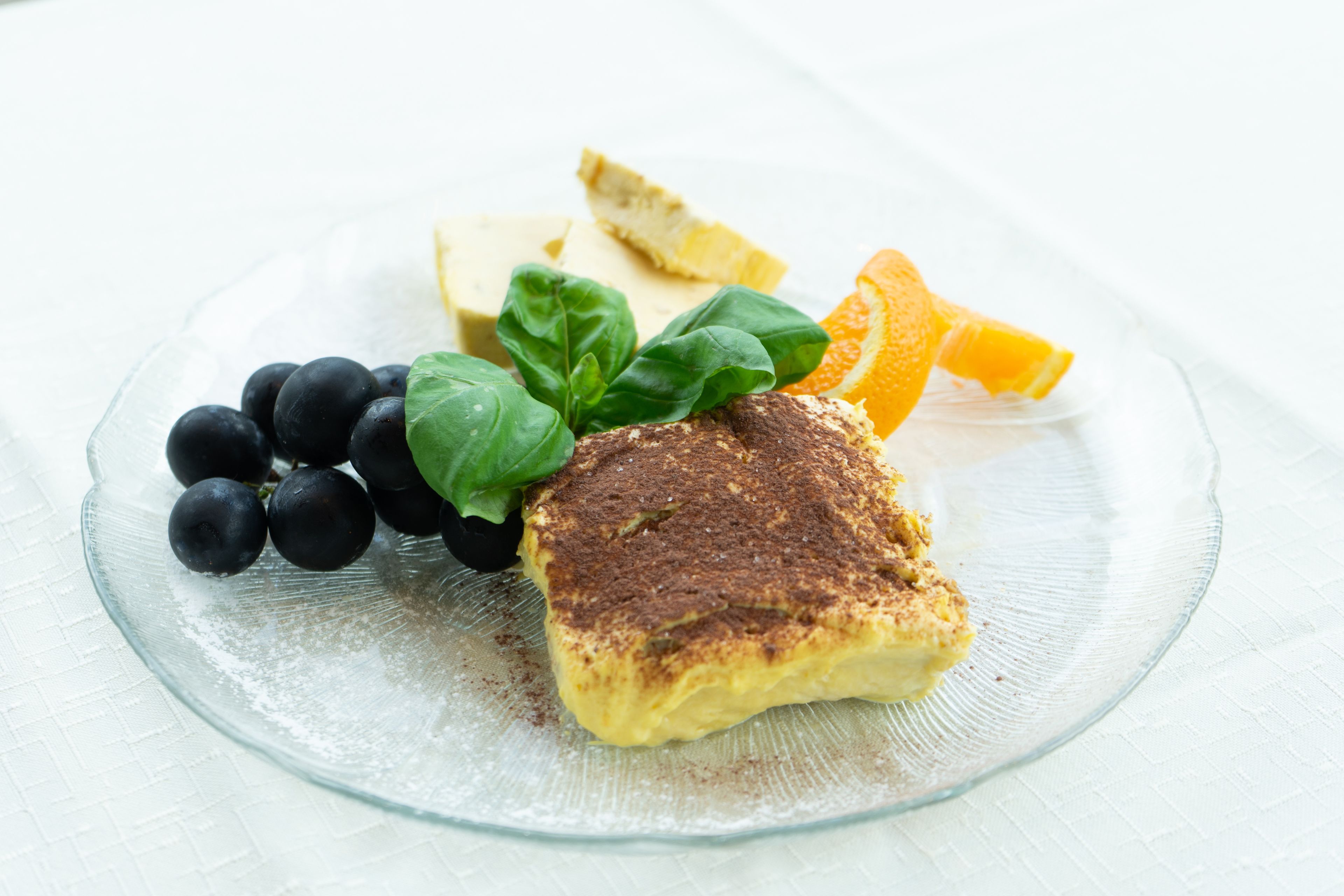 A plate with a slice of cake, blueberries, a lemon, and a basil leaf.