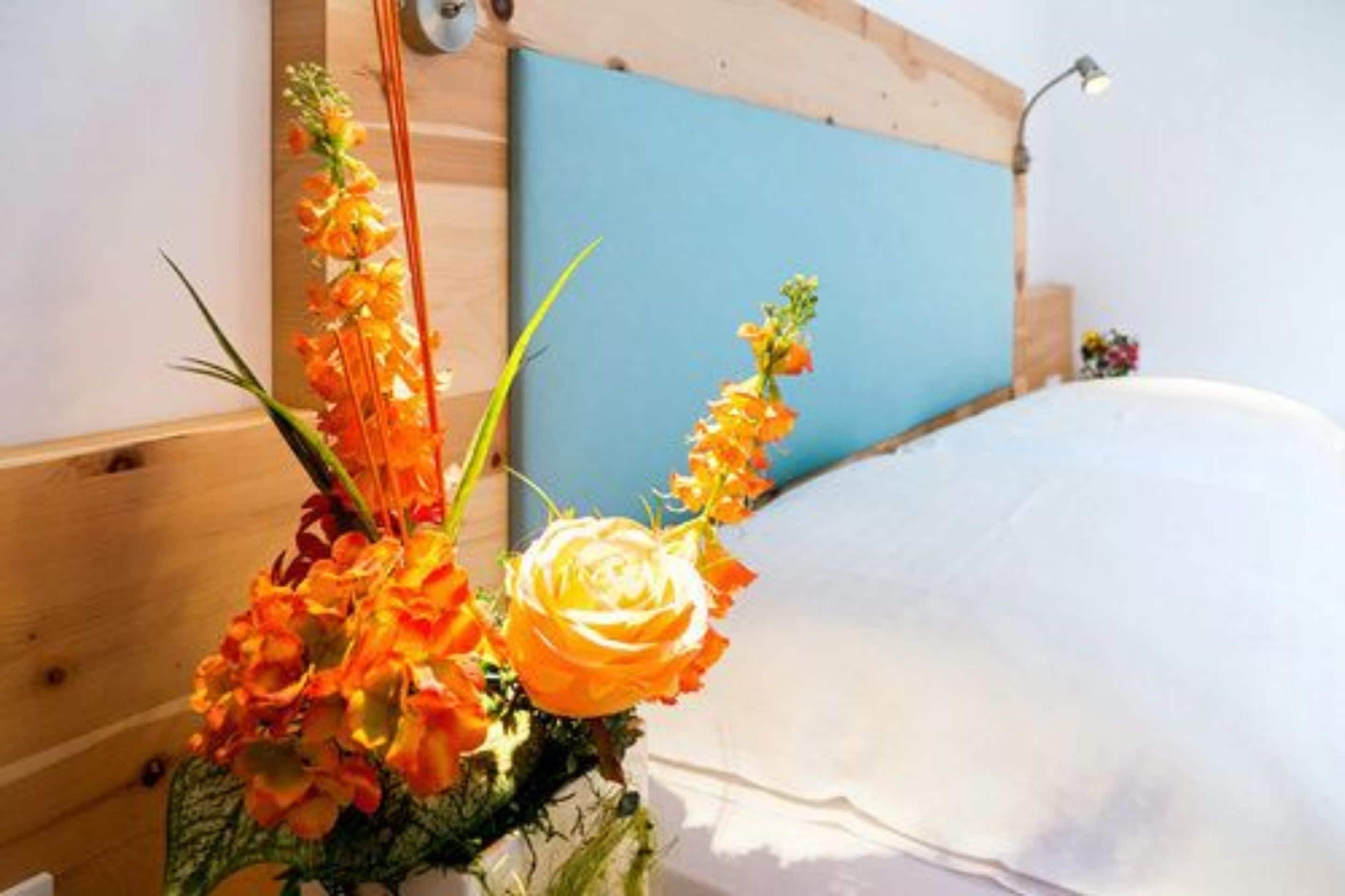 A bed with white bedding, a blue headboard, and a floral arrangement on the side.
