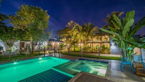 A swimming pool with a tiled deck, surrounded by palm trees and benches, with buildings in the background. - Pousada Gira Sol (Bonito)