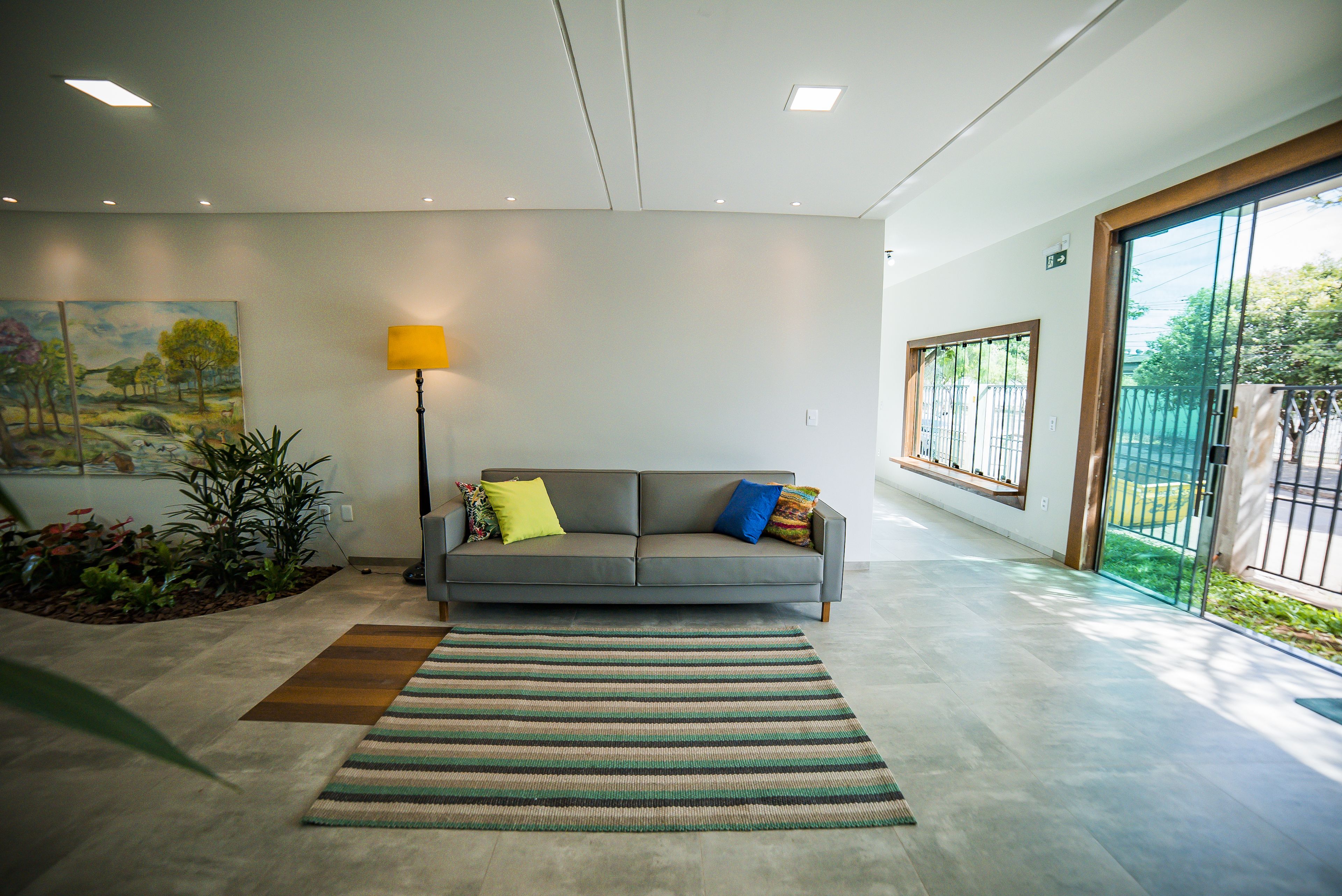 A modern living room with a grey sofa, colorful cushions, a lamp, and a large window.