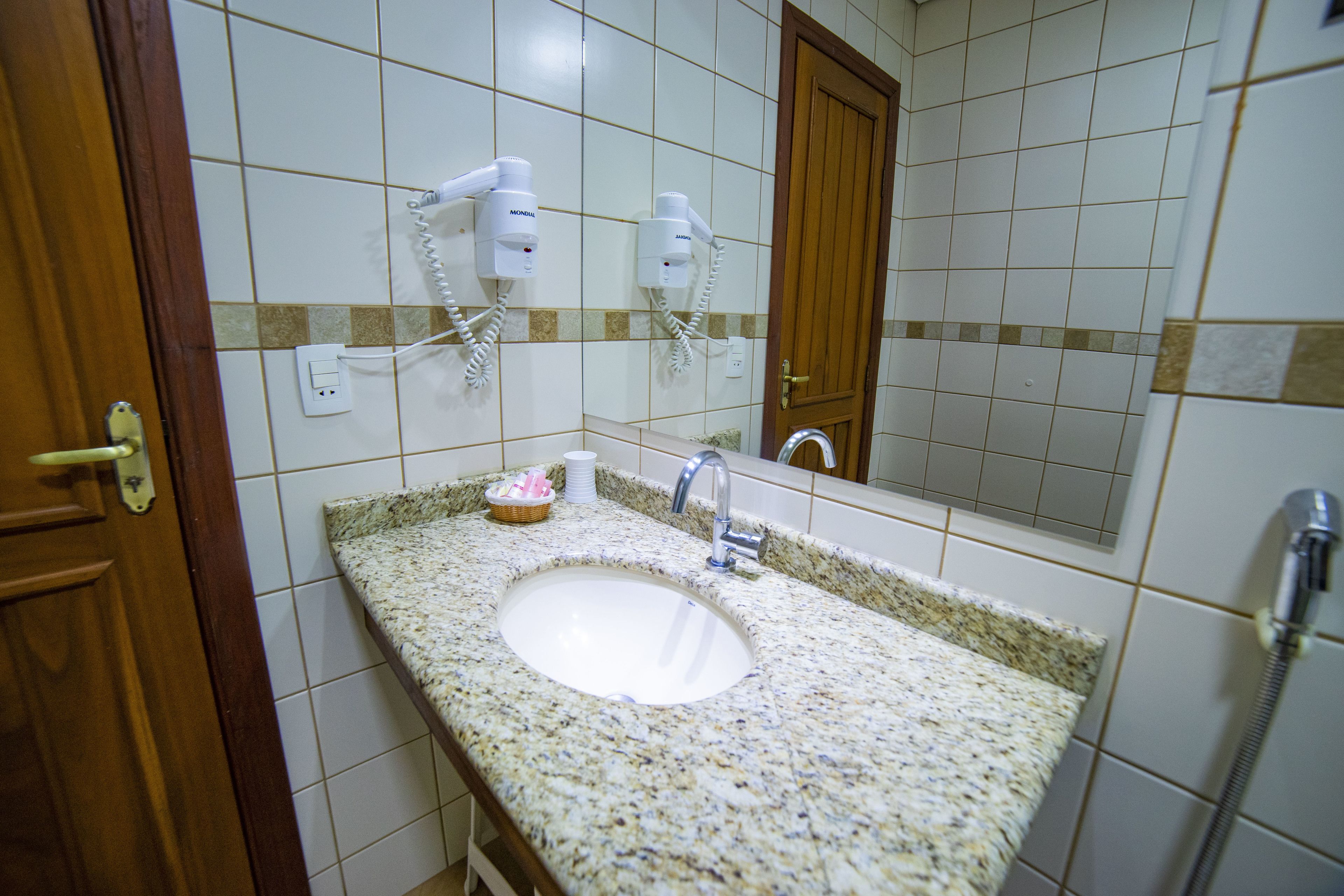 A bathroom with a granite countertop sink, a mirror, a wooden door, and two hair dryers mounted on the wall.