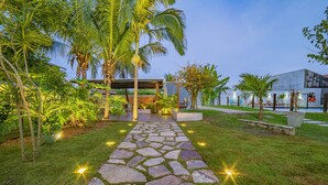 A stone pathway leading to a building with a modern design, surrounded by lush greenery and palm trees. - Pousada Gira Sol (Bonito)