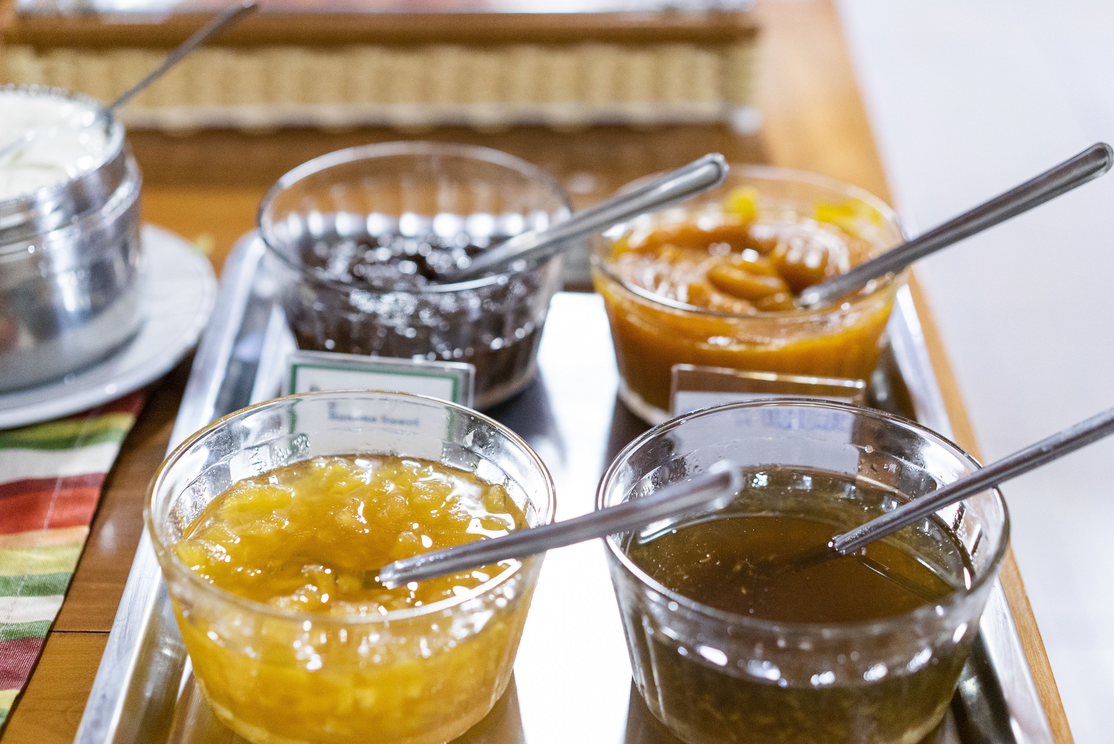 Un plateau contenant quatre récipients en verre remplis de différents aliments, chacun accompagné d’une cuillère.