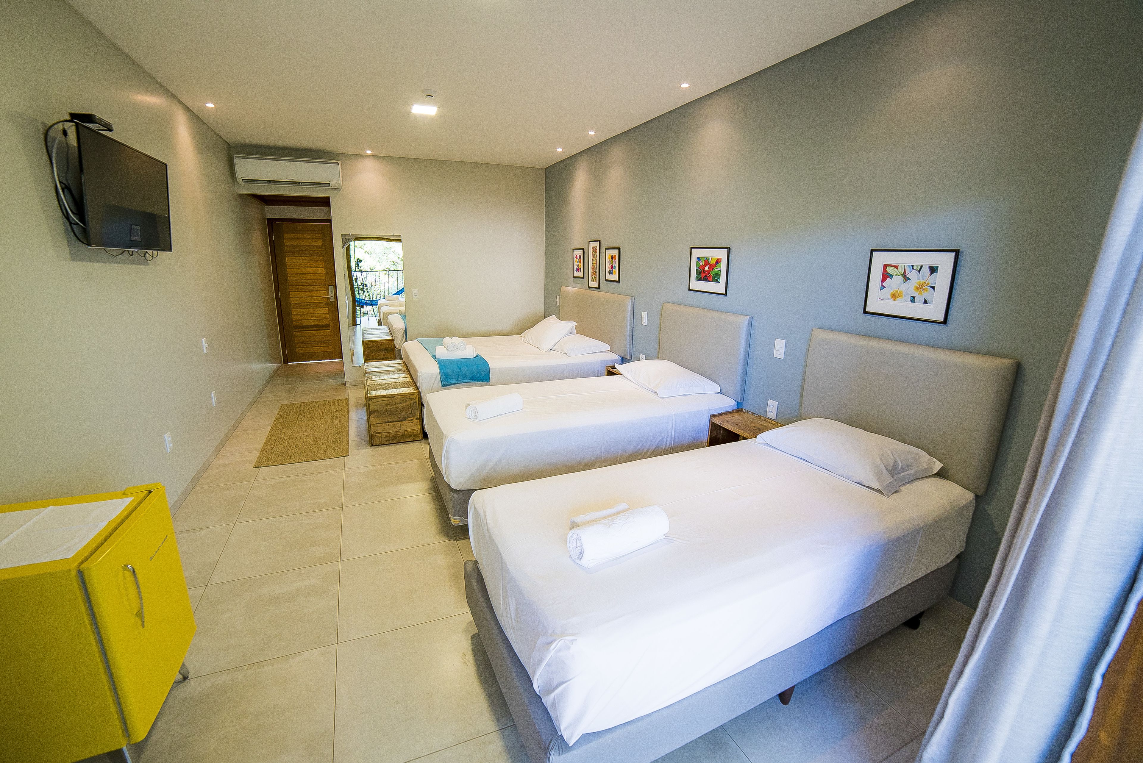 A hotel room with three single beds, a TV, an air conditioner, and a yellow cabinet.
