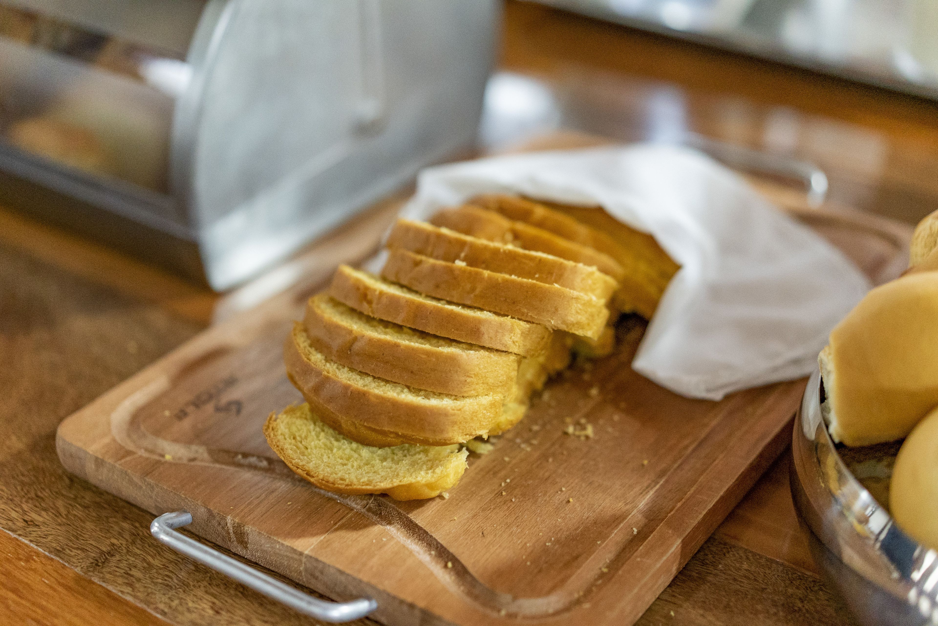 Tábua de corte de madeira com pão fatiado e um recipiente de metal.