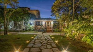 A house with a stone pathway leading to a wooden door, surrounded by lush greenery and outdoor seating. - Pousada Gira Sol (Bonito)