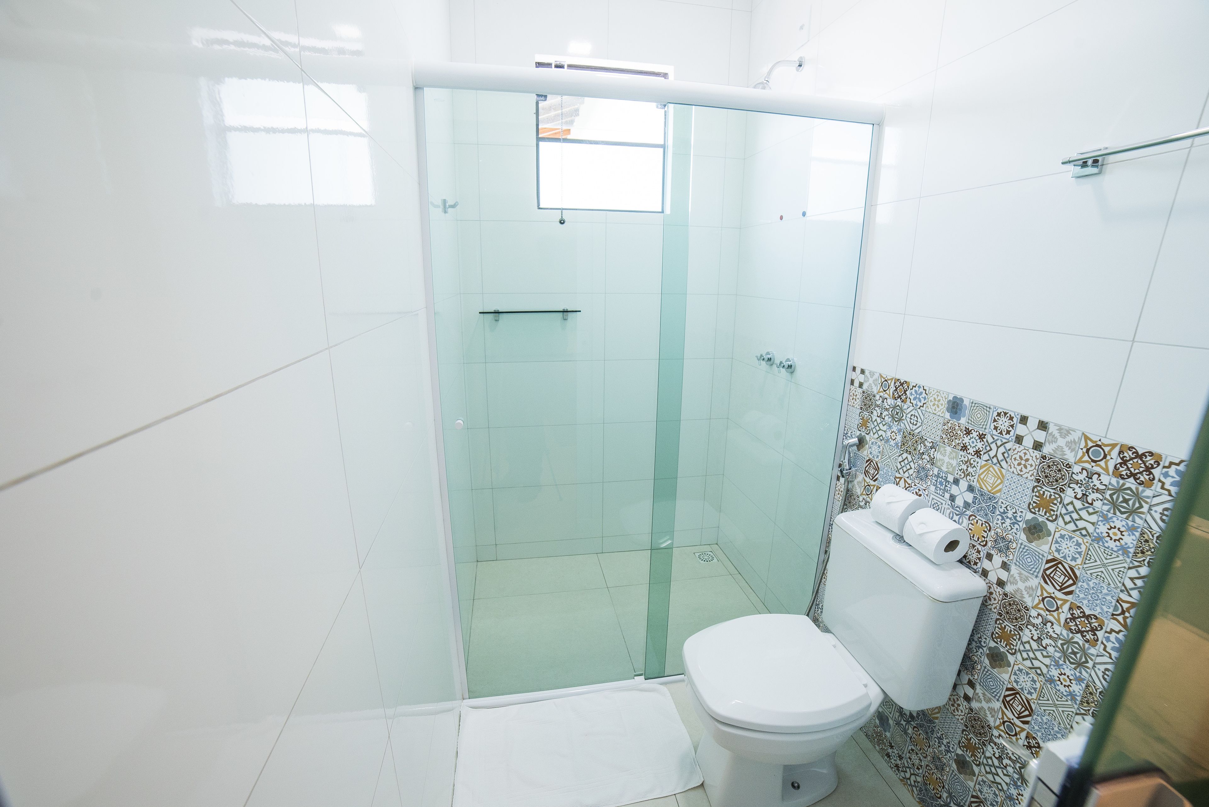 Un baño con ducha envuelta en vidrio, inodoro y pared de azulejos con diseño decorativo.