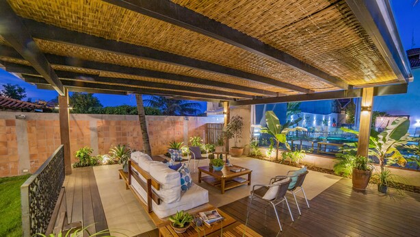 An outdoor patio area with a wooden deck, a covered seating area with a sofa and chairs, and a pool in the background. - Pousada Gira Sol (Bonito)