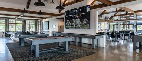 A spacious indoor area with pool tables, wooden beams, and large windows.