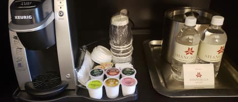 A Keurig coffee maker, a tray with various tea and coffee pods, and two bottles of Shangri-La Resort water.