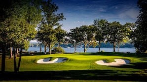 Campo de golf con búnkeres de arena, árboles y un lago al fondo.
