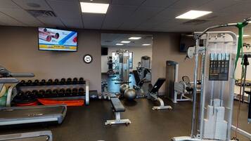 A gym with treadmills, dumbbells, a TV screen, and various exercise equipment.