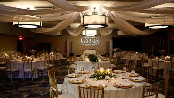 Une salle de banquet avec des tables rondes dressées pour un événement formel, agrémentée de nappes blanches, de touches dorées et d’un éclairage élégant.