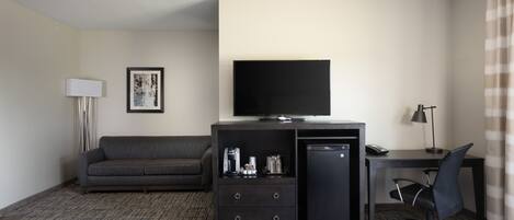 Hotelkamer met flatscreen-tv, een bank, een bureau met stoel en een koffiezetapparaat.