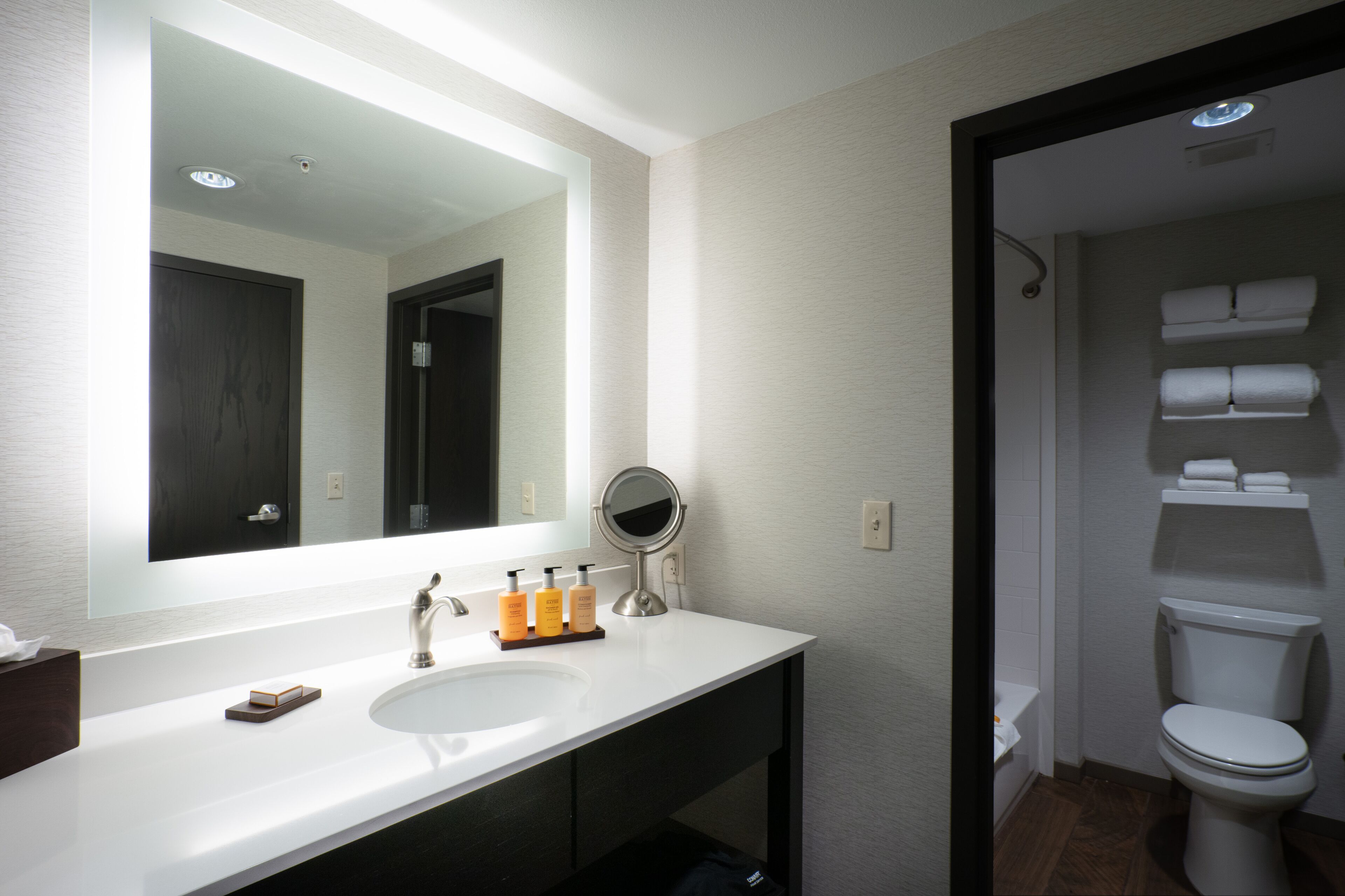 A modern bathroom with a white sink, a large mirror, and a toilet.