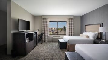 A hotel room with two beds, a desk, a TV, and a view of the city.