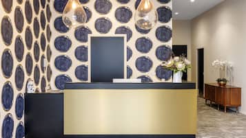 A reception desk with a modern design, a patterned wall, and a potted plant.