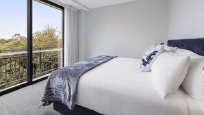 A modern hotel room with a large bed, a view of the outdoors, and a balcony.