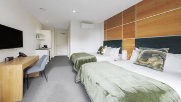 Una habitación de hotel con escritorio, dos camas, televisión y cabecero de madera.