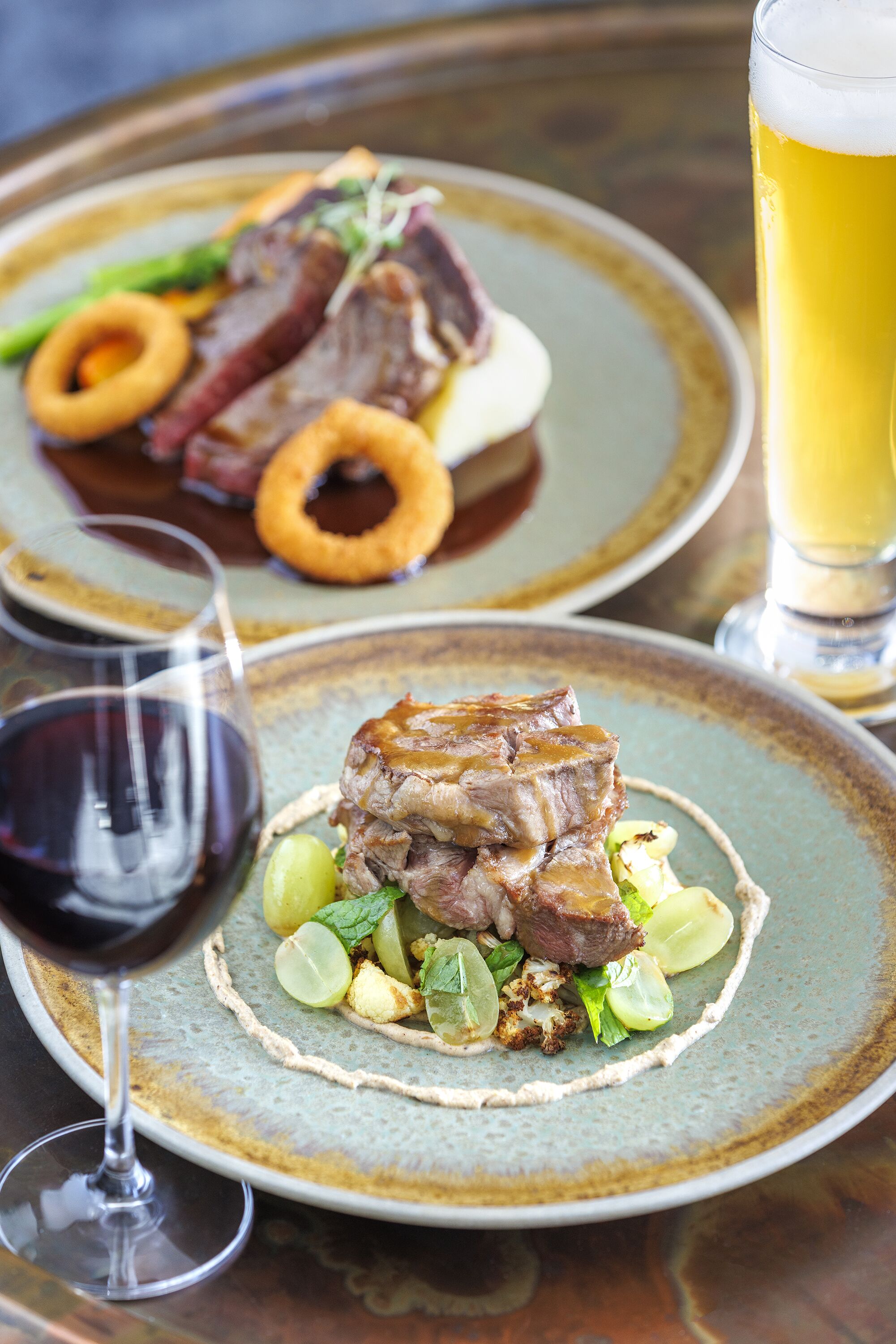 Un tavolo da pranzo con piatti di cibo, un bicchiere di birra e un bicchiere di vino rosso.