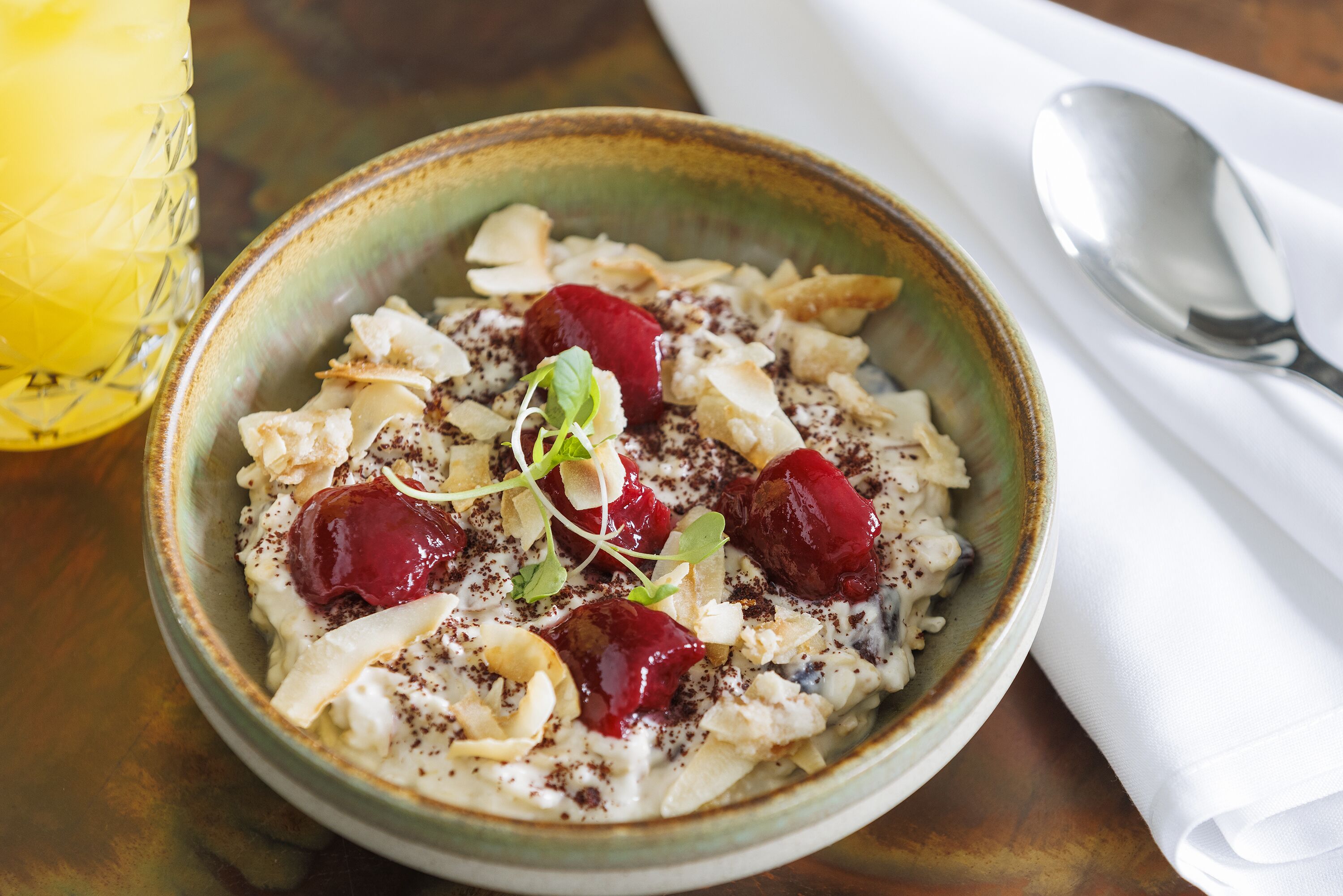 A bowl of oatmeal with cherries and nuts on a wooden table.