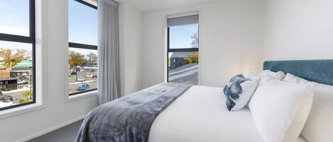 Una habitación de hotel moderna con una cama grande, vistas a la calle a través de amplias ventanas y un cabecero azul.