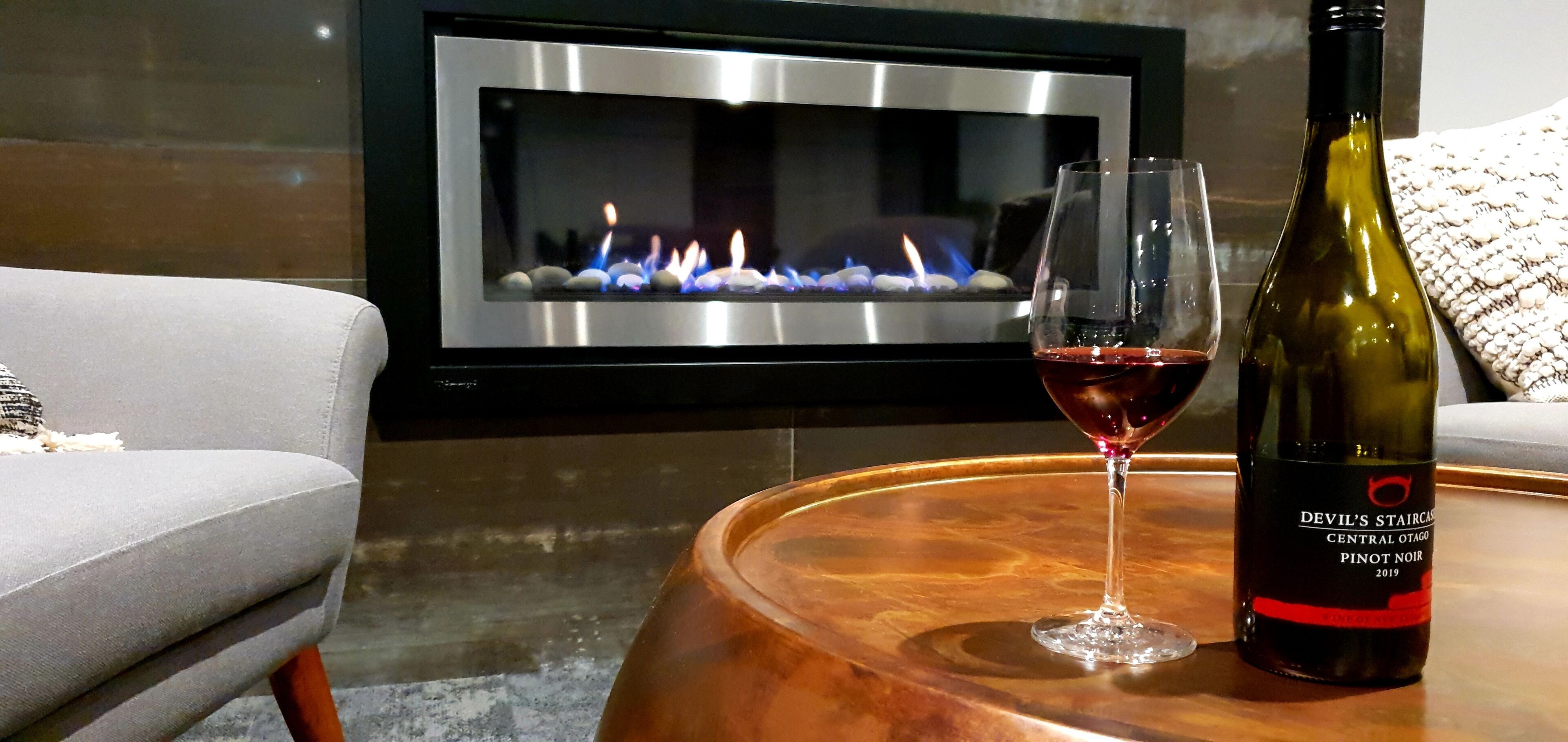 A modern living room with a fireplace, a wine bottle, and a glass of red wine on a wooden coffee table.
