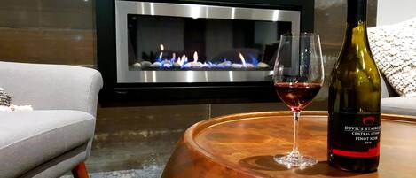 A modern living room with a fireplace, a wine bottle, and a glass of red wine on a wooden coffee table.