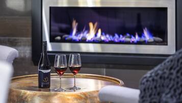 A bottle of wine and two glasses on a round table with a fireplace in the background.