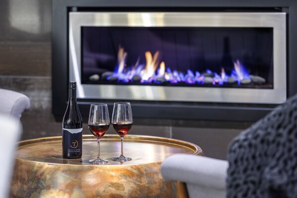 A bottle of wine and two glasses on a round table with a fireplace in the background. - Hidden Lake Hotel and Apartments (Cambridge)