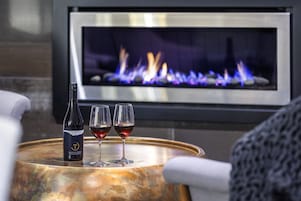Una botella de vino y dos copas sobre una mesa redonda, con una chimenea al fondo.