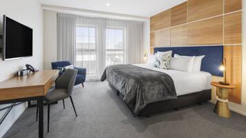 Habitación de hotel con cama, escritorio, silla, televisor y ventana con cortinas.