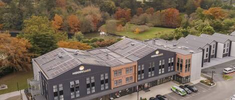 Un bâtiment moderne doté de panneaux solaires, portant l’inscription « Hidden Lake », et offrant un parking ainsi qu’une vue sur un lac et des arbres.