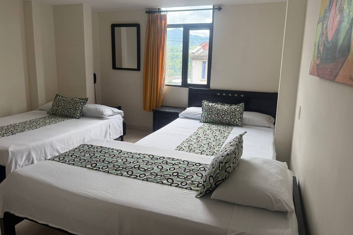 A hotel room with two single beds, a window with curtains, a bedside table, and a wall-mounted mirror.