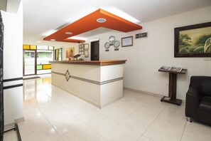 A hotel reception area with a reception desk, a clock, and a framed painting on the wall. - Hotel Los Tunjos (Pereira)