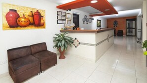 Un espace d’accueil avec un canapé marron, un comptoir de réception et un tableau représentant des poteries accroché au mur.