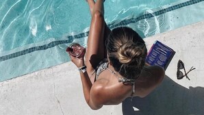 A person relaxing by a pool with a book and a drink.